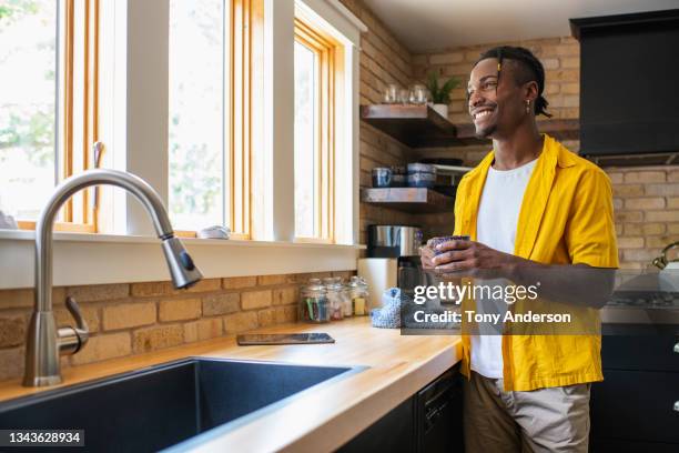 young man standing at kitchen counter holding mug - letting it all hang out stock pictures, royalty-free photos & images