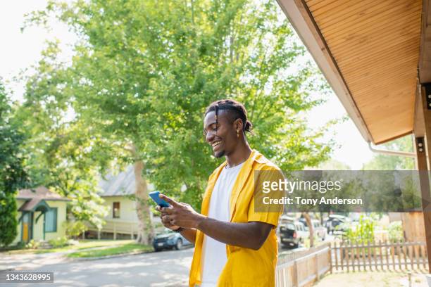 young man standing in yard of his house using phone - yellow shirt stock pictures, royalty-free photos & images