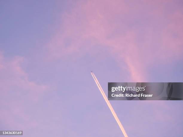 an aeroplane or airplane flies through the sky at sunset - sunset contrail stock pictures, royalty-free photos & images