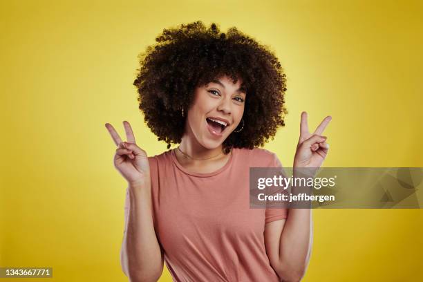 scatto in studio di una giovane donna attraente che fa un gesto di pace su uno sfondo giallo - esprimere a gesti foto e immagini stock