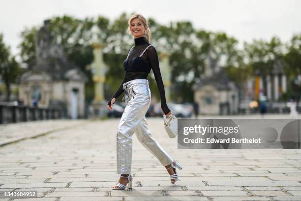 Xenia Adonts wears a black transparent turtleneck long sleeves t-shirt, a black bra underwear with silver and rhinestones chain shoulder, high waist...