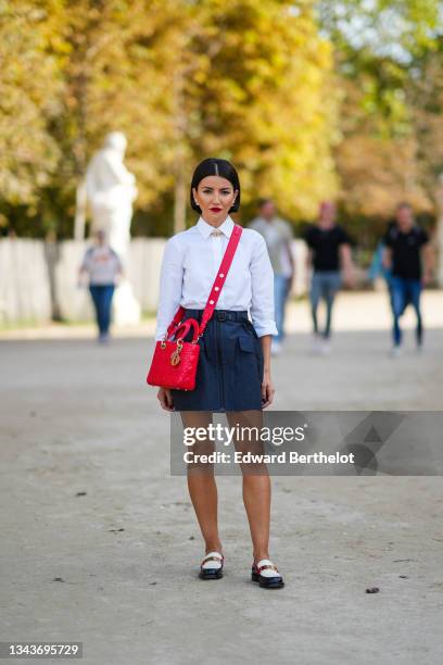 Alexandra Pereira wears gold and pearl earrings, a white shirt, a gold large chain CD necklace from Dior, a crafted in red calfskin with cannage...