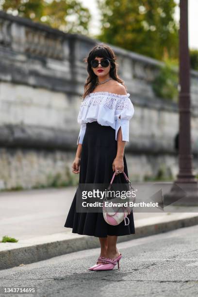 Maria Bernad wears sunglasses, a silver chain necklace, silver earrings, a white cut-out pattern shoulder-off shirt, a high waist flowing midi skirt,...