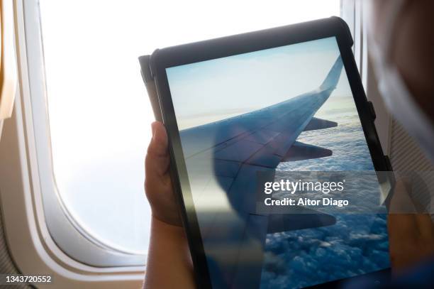 person's hand asking a picture or a video with  a tablet inside an airplane window while in flight. - holds a news conference in berlin stockfoto's en -beelden