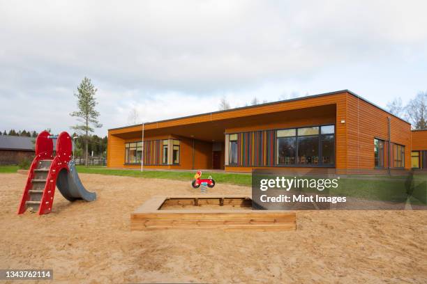 a modern building, nursery or pre-school, a large sand pit play area with a slide. - school building exterior stock-fotos und bilder