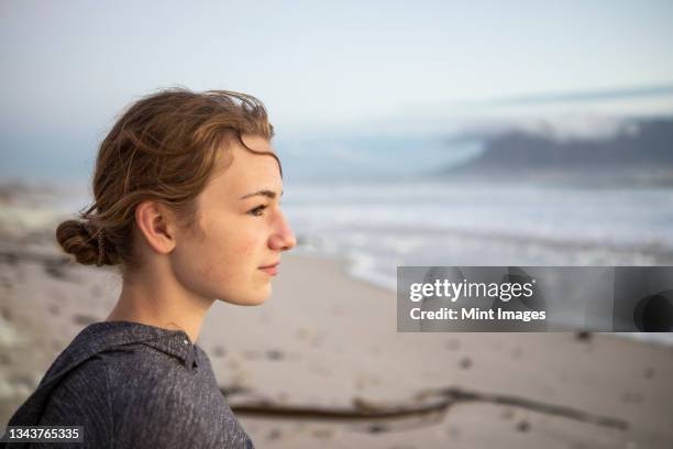 profile of a teenage girl looking out to sea from a beach at sunset. - young teen girl beach stock pictures, royalty-free photos & images