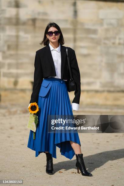 Guest wears black sunglasses, gold earrings, a white shirt, a black cropped blazer jacket, a black shiny leather shoulder bag, a blue high waist...