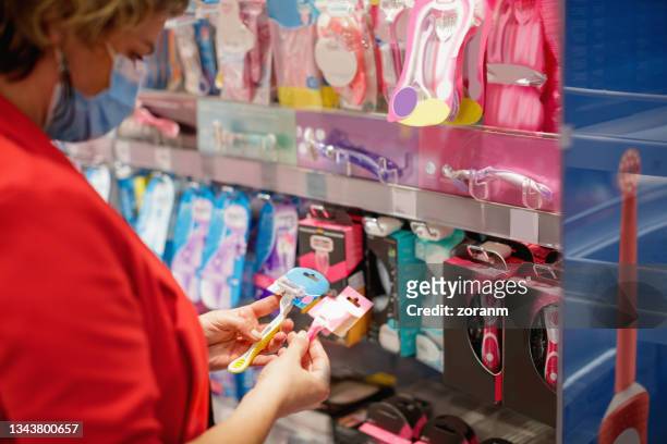 woman comparing shaving razors by the shelf in the supermarket, making up her mind - lâmina de barbear imagens e fotografias de stock