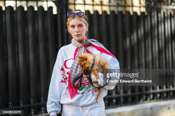 Guest wears sunglasses, a beige and brown monogram print pattern with red borders silk scarf from Gucci, a white with green / red / black print...