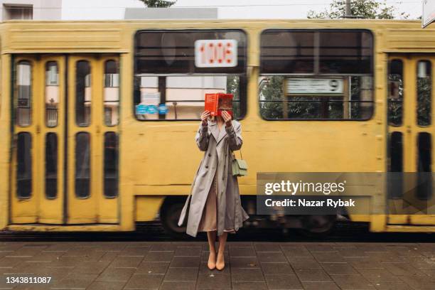 a beautiful woman in a trench standing on the tram background - trench town stock pictures, royalty-free photos & images