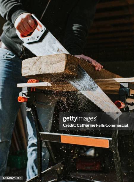 a man uses a handsaw to cut a thick piece of wood - sawdust stock pictures, royalty-free photos & images