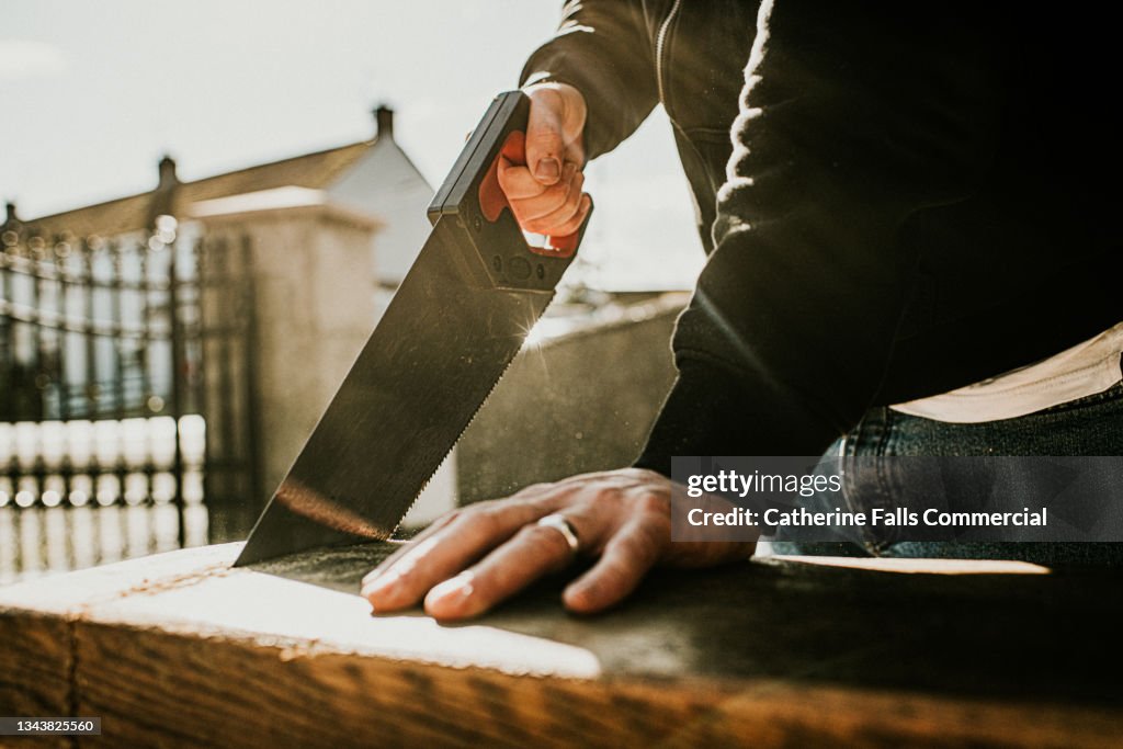 Back-lit close-up of a man using a handsaw