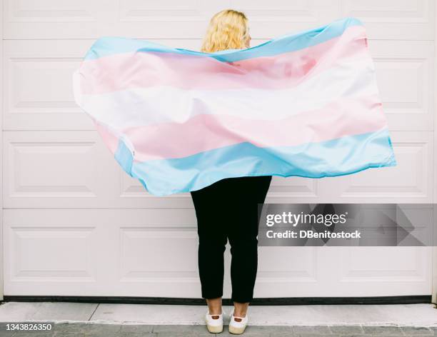 transgender person from behind, wearing pink and white striped sweatshirt, holds transgender flag - transgender bildbanksfoton och bilder