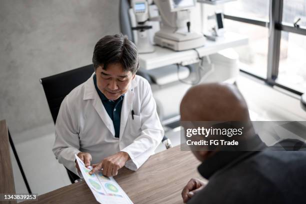 médico hablando con el paciente que muestra exámenes de la vista durante la cita médica - ophthalmologist fotografías e imágenes de stock