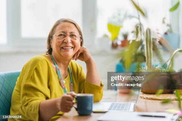 porträt einer glücklichen modischen seniorin, die für die kamera lächelt, während sie den laptop zu hause benutzt - elder woman stock-fotos und bilder