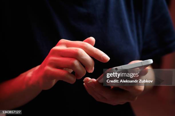 a mobile phone in the hands of a girl. a young woman in a black t-shirt is holding a phone. the fraudster sends an email message. the work of a freelancer, businessman. the wife checks messages and notifications on social networks. wireless technologies. - usar el teléfono fotografías e imágenes de stock