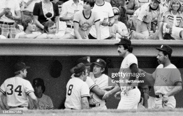 Yankees' manager Billy Martin comes up off the dugout bench to confront right fielder Reggie Jackson who is coming into the dugout after being lifted...