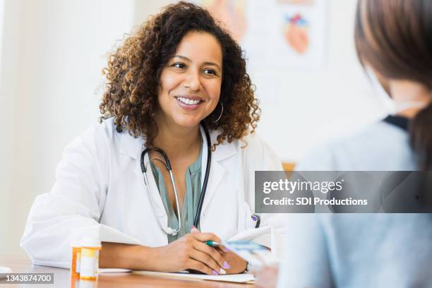 mid adult female doctor smiles encouragingly at unrecognizable female patient - gynecologist stock pictures, royalty-free photos & images