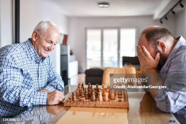 father smiling at son worried about losing chess game - chess defeat stock pictures, royalty-free photos & images