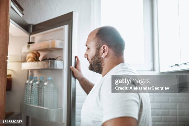 glatzenkopf männlicher öffnen kühlschrank in der küche, um nach essen zu suchen - male stomach stock-fotos und bilder