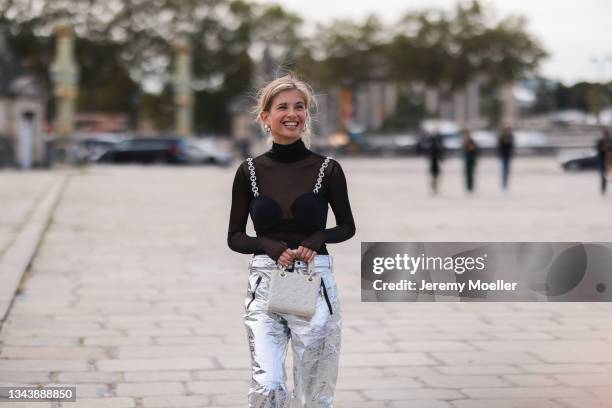 Xenia Adonts wearing a black, transparent shirt, silver pants and a white dior bag outside Dior on September 28, 2021 in Paris, France.
