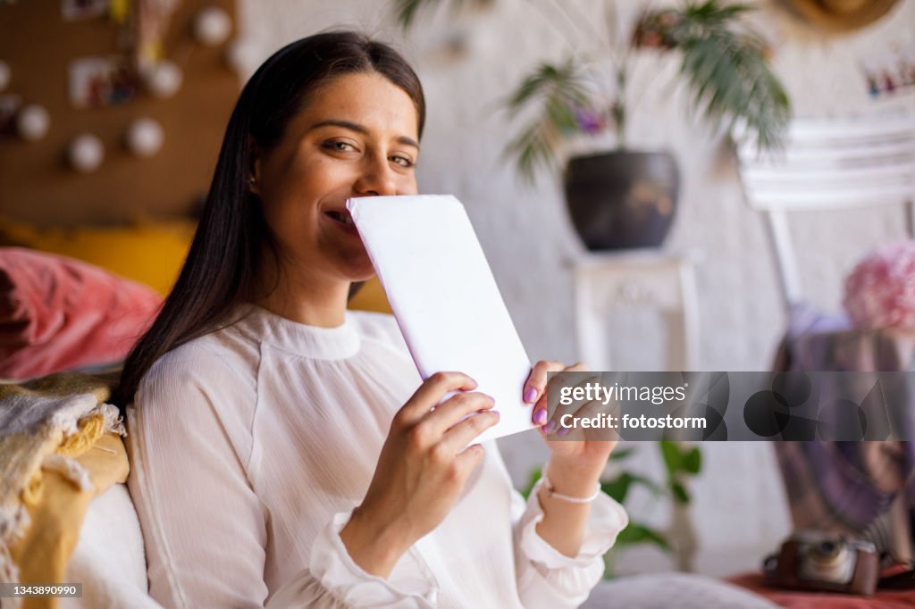 Cheerful young woman hiding her smile behind a love letter from a crush