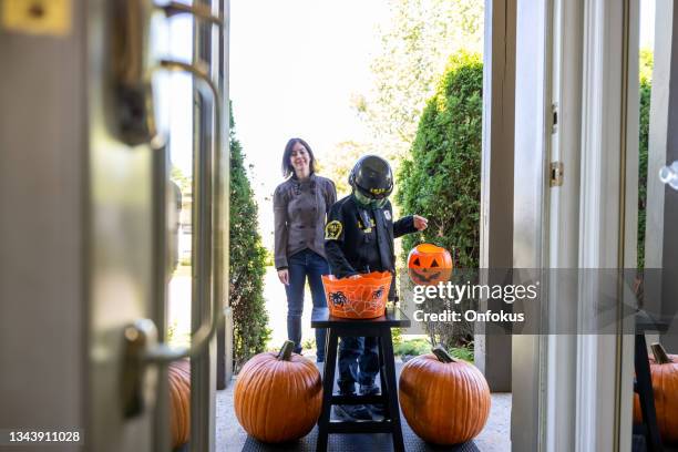 young boy wearing a police officer costume is taking candies on halloween at front door of a house - halloween covid stock pictures, royalty-free photos & images