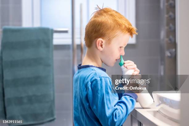 小さな赤毛の少年は、生理的な鼻スプレーで彼の鼻を掃除し、空に - 生理食塩水 ストックフォトと画像