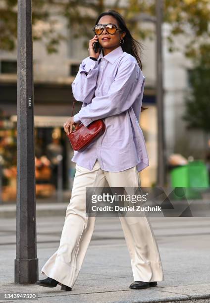 Guest is seen wearing a purple shirt and white pants with red bag outside the Acne show during Paris Fashion Week S/S 2022 on September 29, 2021 in...