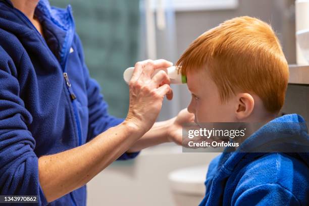 mother measuring temperature of his sick boy with infrared thermometer - infrared thermometer stock pictures, royalty-free photos & images