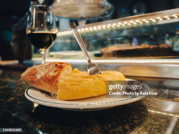 slice of potato omelette (spanish "tortilla de patatas") with some bread and red wine on the bar counter. - tortilla de patata fotografías e imágenes de stock