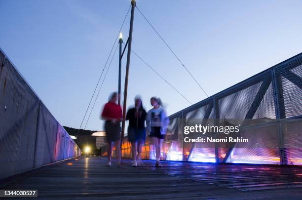 three female friends walking on wellington harbour footbridge at dusk - wellington nz fotografías e imágenes de stock