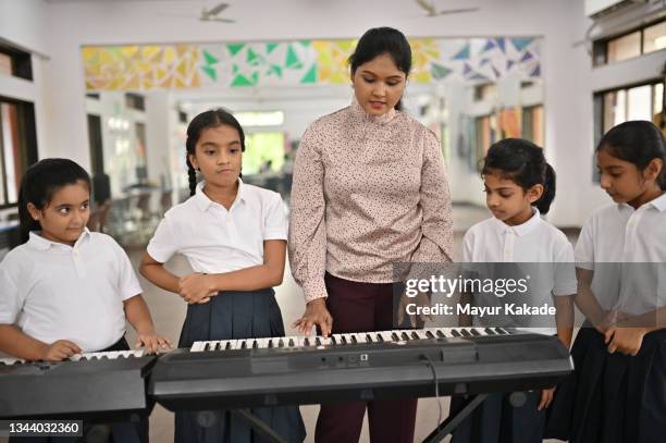 school children learning to play keyboard musical instrument with their teacher in music room - keyboard musical instrument child stock-fotos und bilder