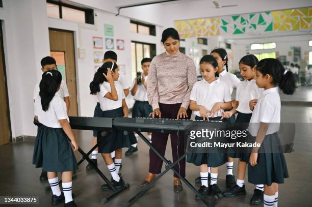 school children learning to play keyboard musical instrument with their teacher in music room - keyboard musical instrument child stock-fotos und bilder