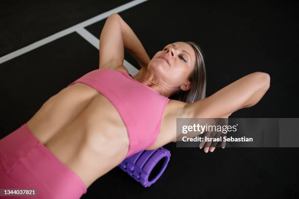 athlete woman massaging her back with a foam roller after hard workout at the gym. - massage ball stock pictures, royalty-free photos & images