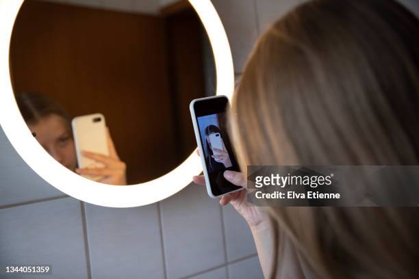 close up of a teenage girl taking a self portrait of her reflection in an illuminated mirror using a mobile phone. - gesundheitsbewußt stock-fotos und bilder