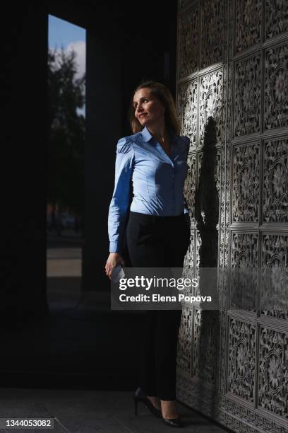 young beautiful business woman with smartphone leaving office building - corporate dark portrait stock-fotos und bilder