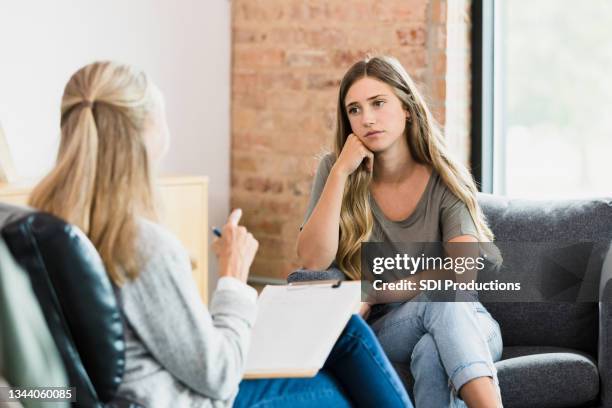 hopeless teen girl listens to advice from unrecognizable female therapist - psychotherapy imagens e fotografias de stock