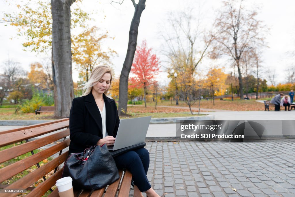 Frau benutzt Laptop, während sie auf der Parkbank sitzt