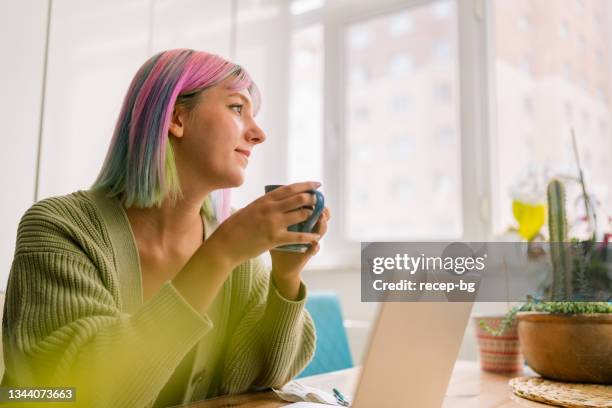 portrait of young woman holding cup of hot drink and looking outside through window - coffee cup top view stock pictures, royalty-free photos & images