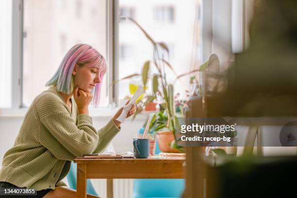 young woman using laptop while drinking hot drink at home - thinking for investment stock pictures, royalty-free photos & images
