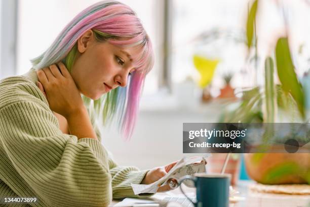 young woman using laptop while drinking hot drink at home - student loan stockfoto's en -beelden