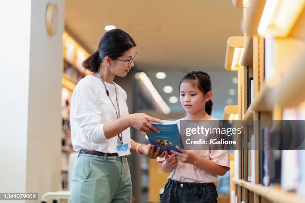 librarian helping a young girl to search for a book - librarian stock pictures, royalty-free photos & images