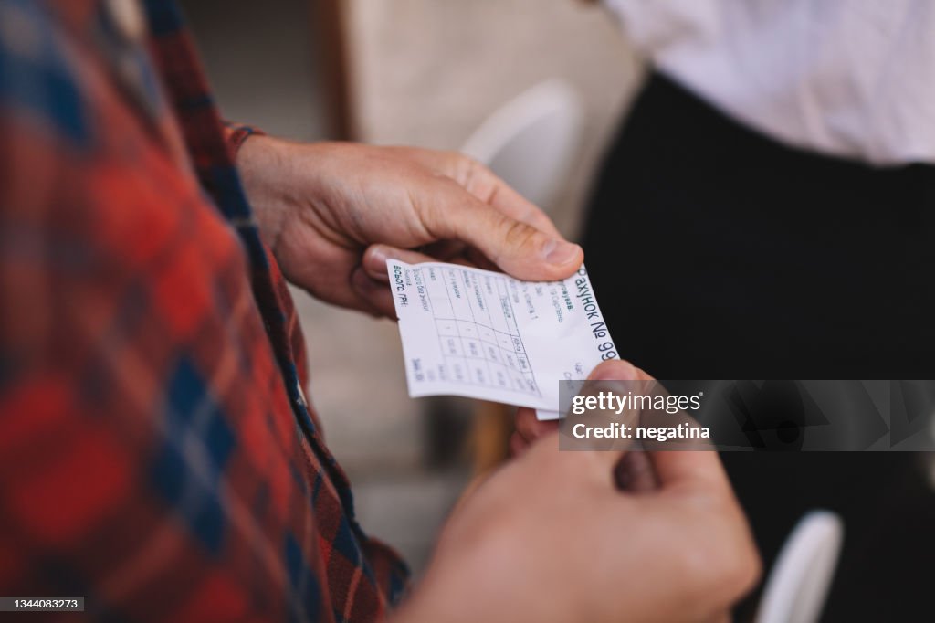 Hands of the young man holding receipt from the restaurant