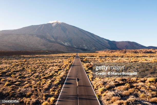 man walking on a straight road towards teide volcano - tenerife stock-fotos und bilder