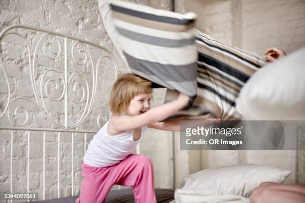 happy mother and daughter having a pillow fight in bed at home - pillow fight stock pictures, royalty-free photos & images