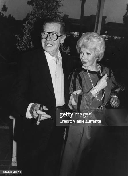 American comedian Milton Berle , holding a lit cigar, and his wife Ruth Cosgrove , wearing a long necklace, location unspecified, circa 1985.