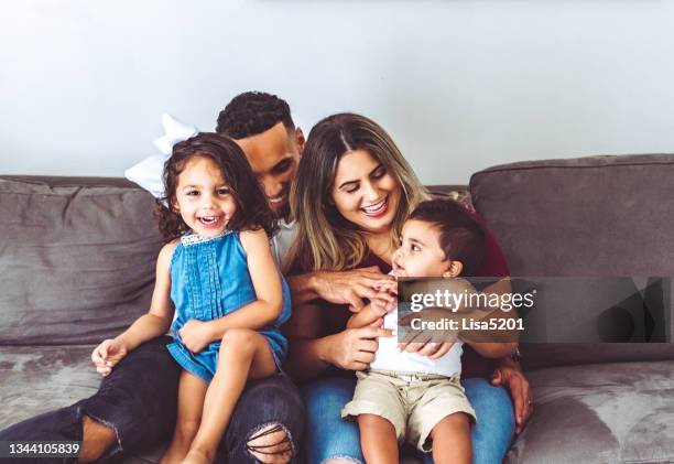 famiglia multirazziale felice a casa con due bambini piccoli in ritratto casuale sul loro divano - mixed race person foto e immagini stock