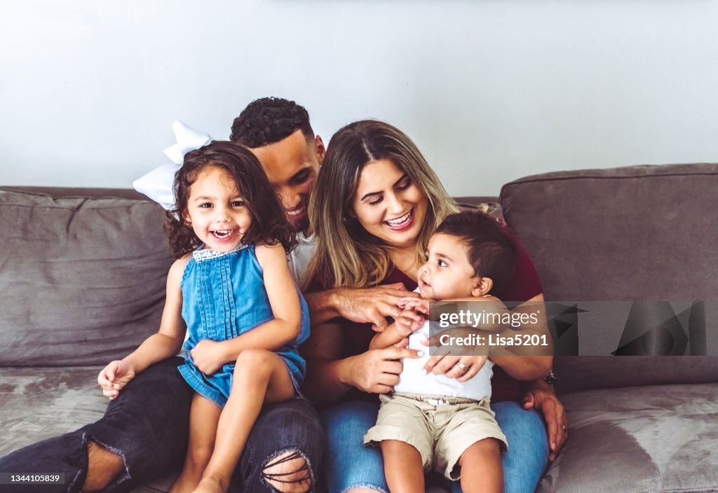 Família multirracial feliz em casa com duas crianças pequenas em retrato casual em seu sofá