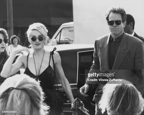 American singer-songwriter and actress Madonna, wearing sunglasses with a black dress, with a crucifix hanging from her neck, and American actor and...
